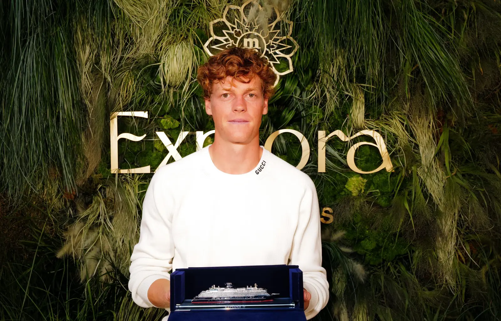 Jannik Sinner holding a model of an Explora Journeys cruise ship at a branded event, highlighting his partnership with the luxury cruise line.