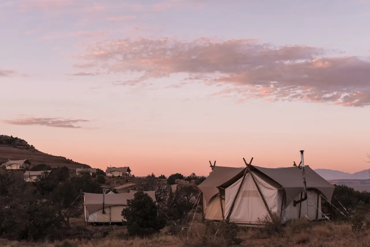 Luxury safari-style glamping tents at sunset in a desert landscape, part of an upscale outdoor retreat similar to Under Canvas or ULUM Moab.