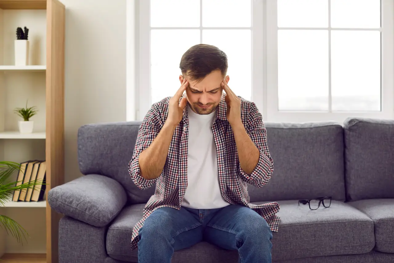 Man sitting on a sofa holding his temples with a severe headache at home
