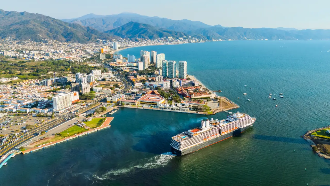 Luxury cruise ship departing Puerto Vallarta marina with city skyline and mountains in the background