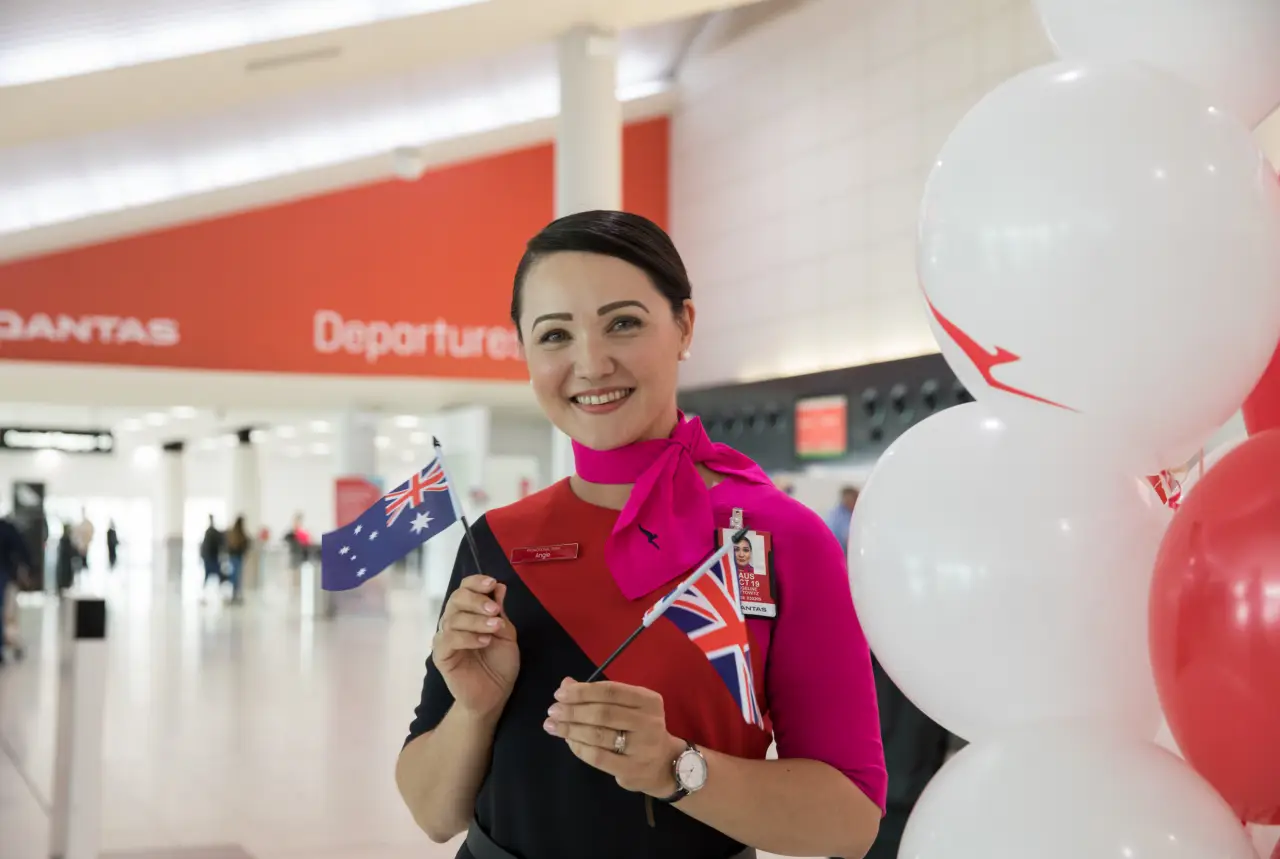 Qantas cabin crew member holding Australian and UK flags at airport departure area