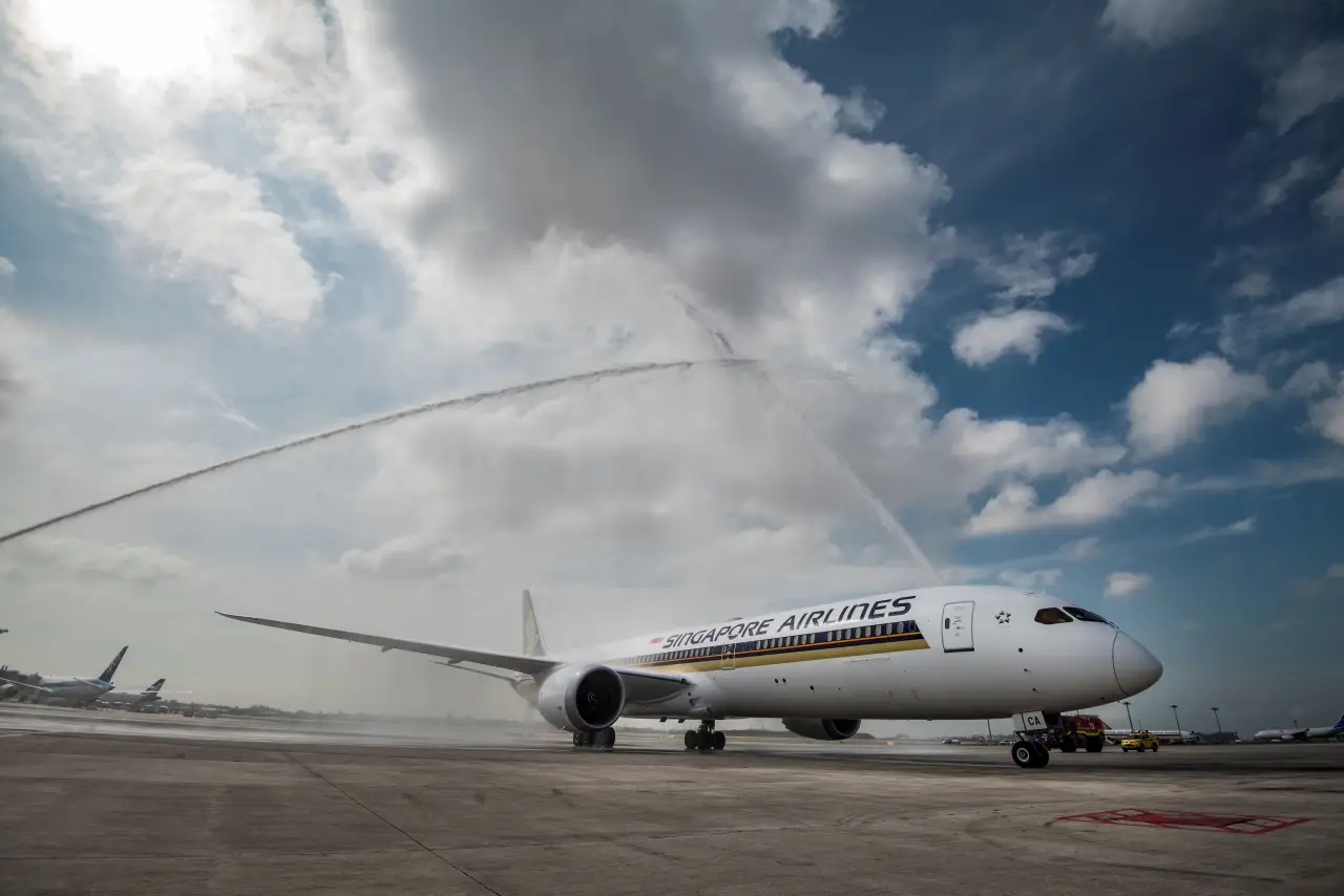 Singapore Airlines Boeing 787-10 receiving water cannon salute on airport runway under partly cloudy sky