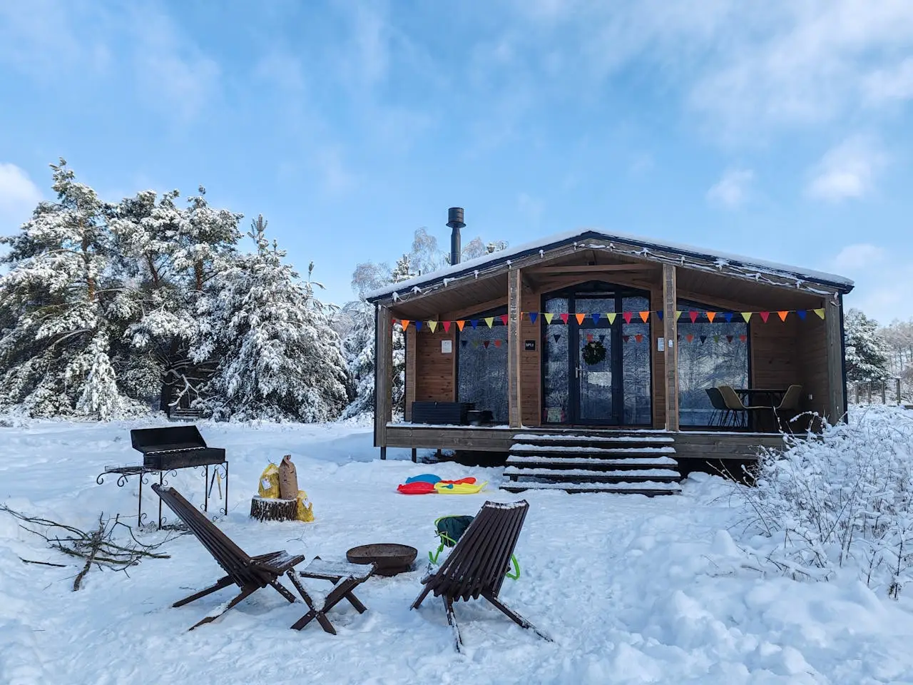 Snow-covered holiday cabin with outdoor seating, barbecue grill, and forest surroundings in winter