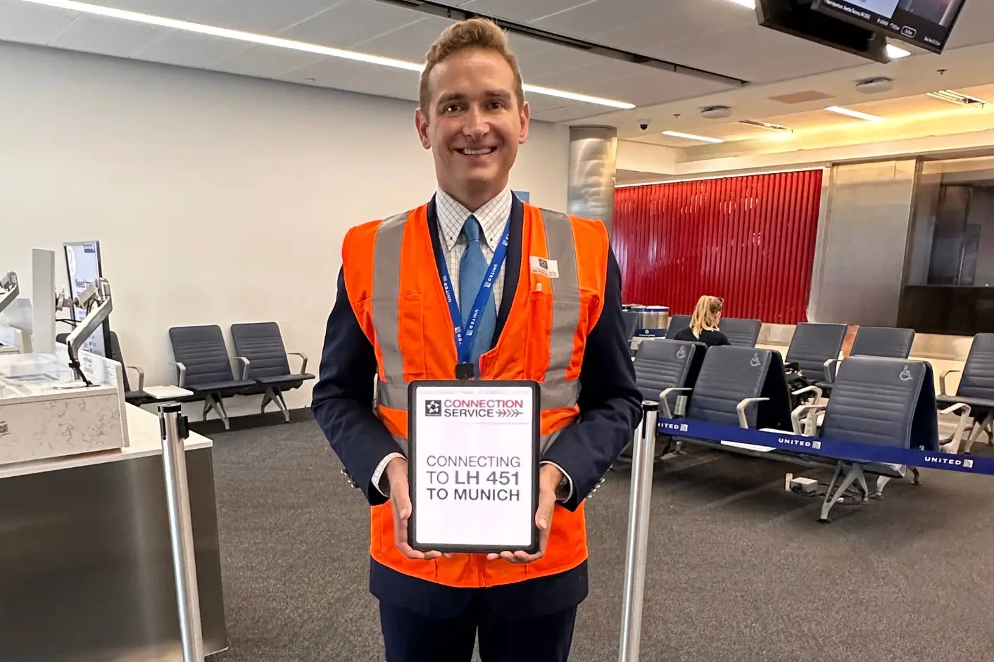 Airport staff member holding a connection service sign assisting passengers with flight transfers at LAX terminal