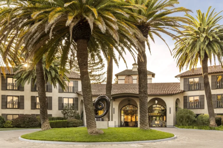Front facade of Casa Mani Resort Napa Valley with tall palm trees, arched entrance and landscaped driveway in downtown Napa.