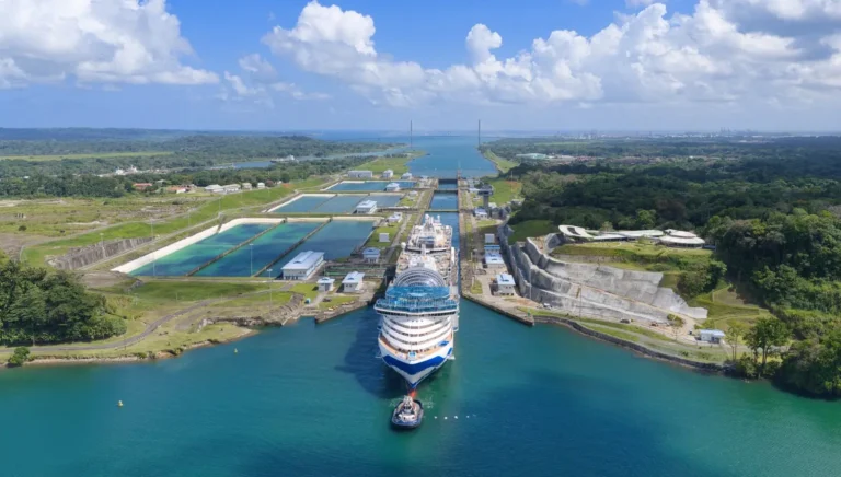 Aerial view of Star Princess cruise ship being guided by a tugboat into the Panama Canal lock system, surrounded by green tropical landscape and blue waters