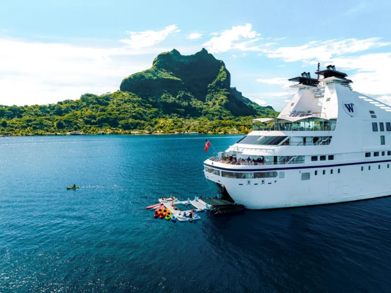 Windstar Star Breeze yacht anchored near Bora Bora with guests kayaking in turquoise waters and lush island mountains in background