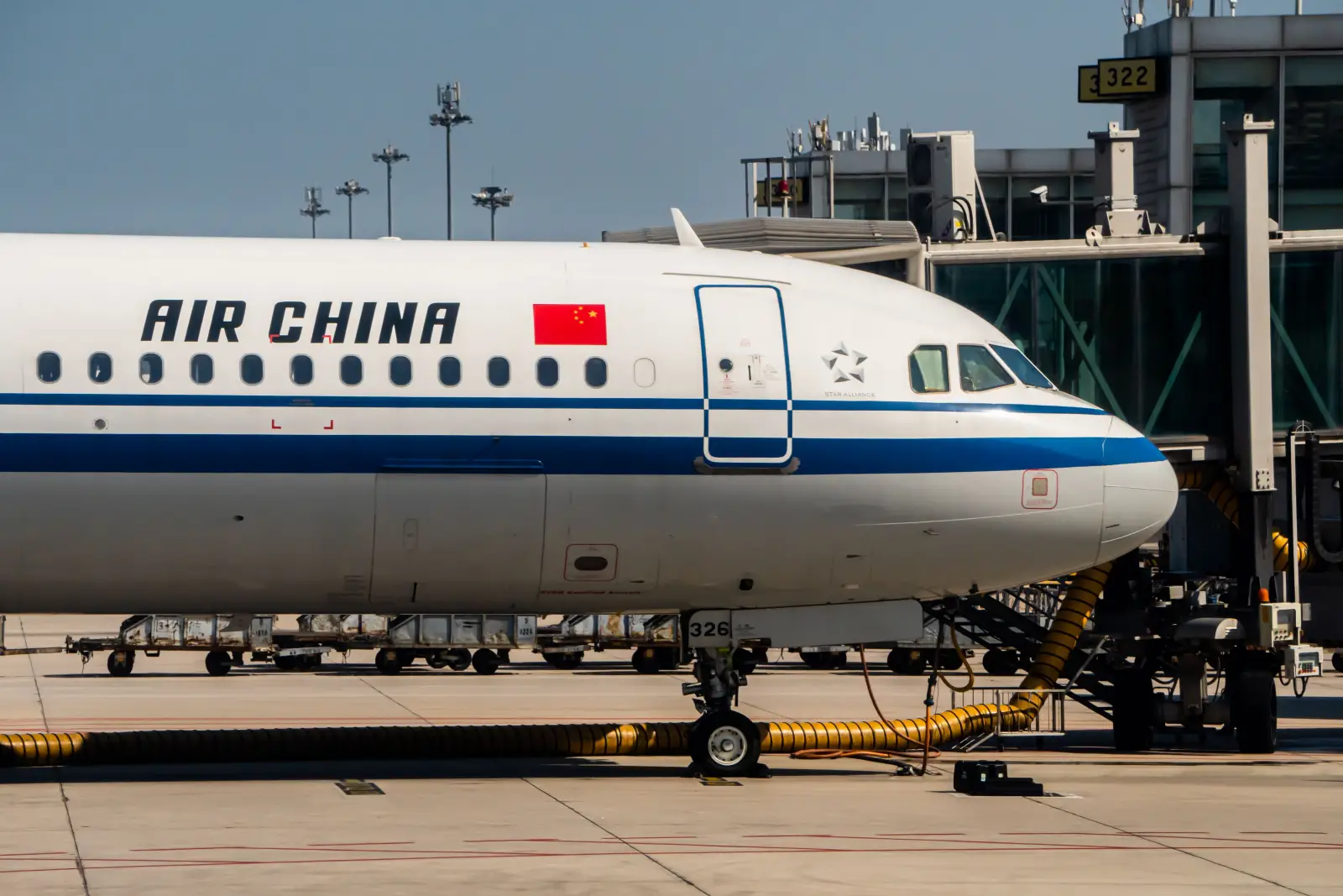 Air China aircraft parked at airport gate with jet bridge attached and ground service equipment visible