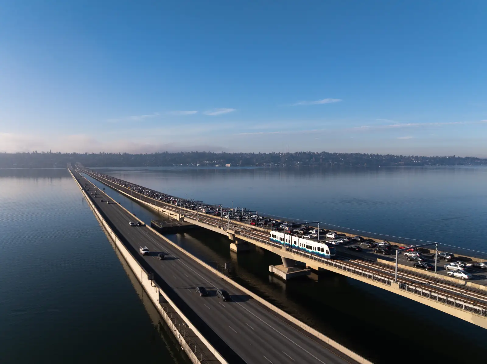 Light rail train crossing floating bridge over Lake Washington between Bellevue and Seattle with cars on adjacent lanes