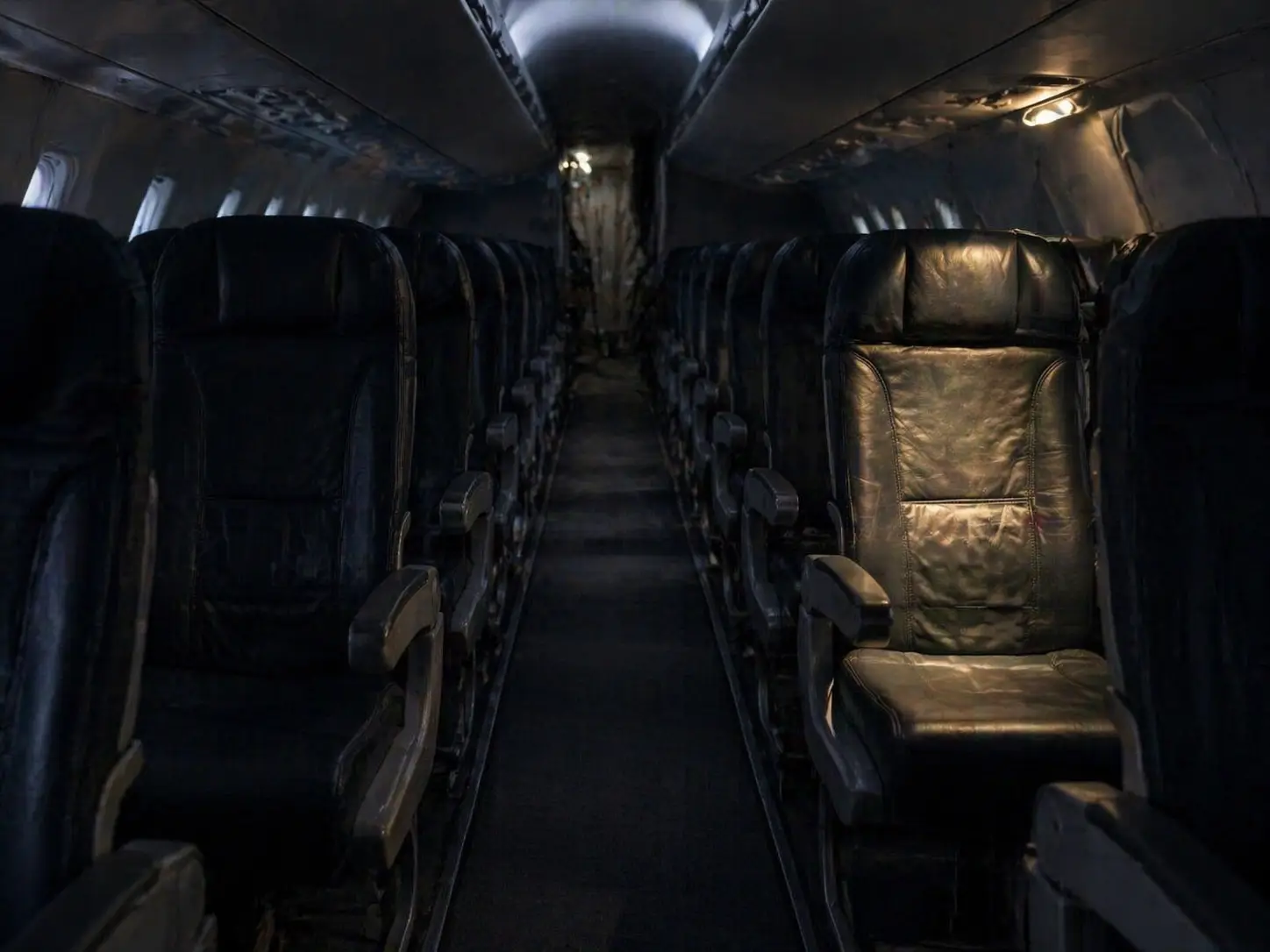 Empty aircraft cabin with dim lighting and a single illuminated seat creating a tense, isolated atmosphere