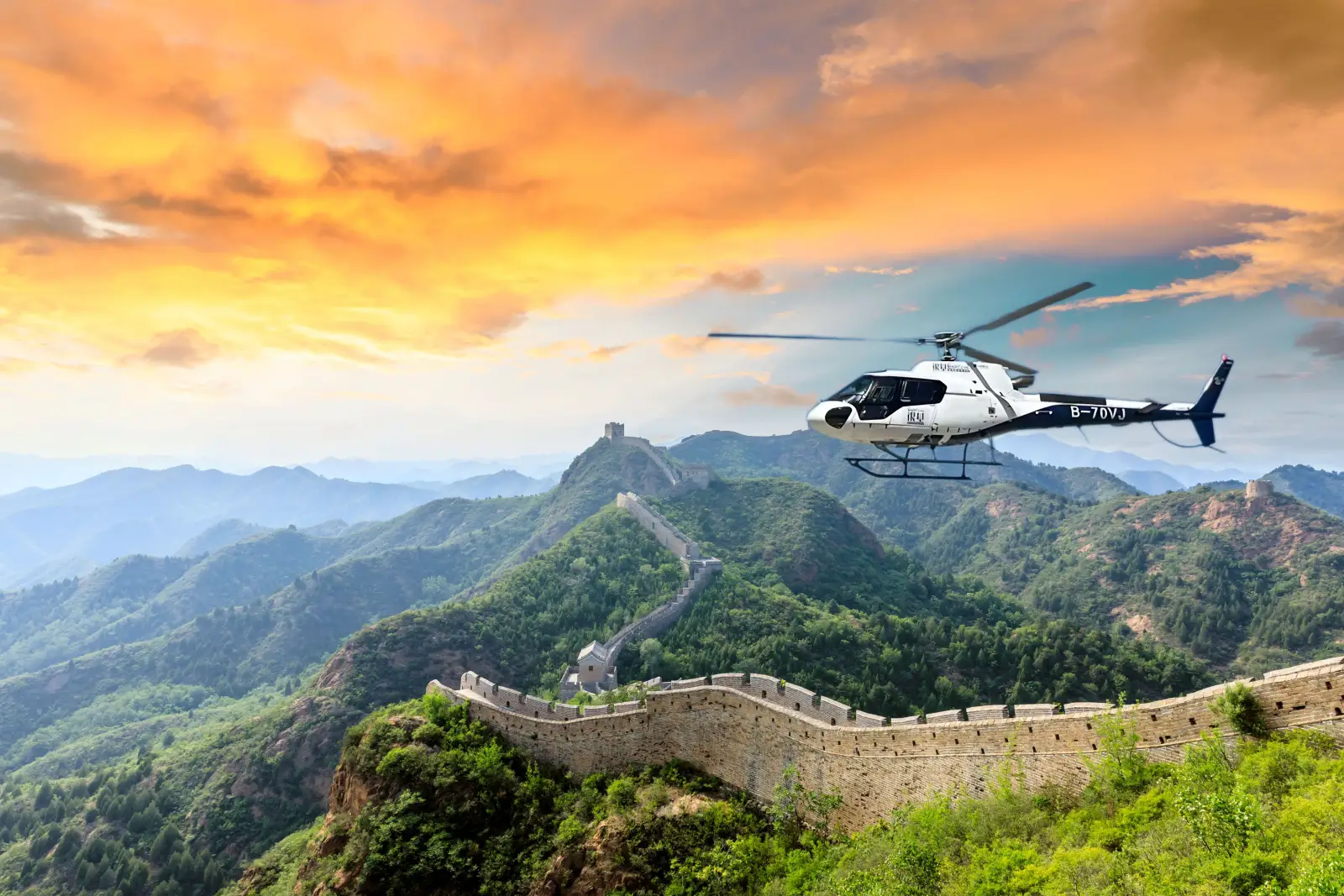 Helicopter flying over the Great Wall of China at sunset with mountain landscape, showcasing a luxury aerial travel experience