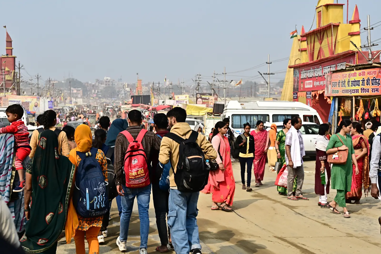 Crowds of pilgrims and backpackers walking through a busy Kumbh Mela festival site with tents and temple structures in India