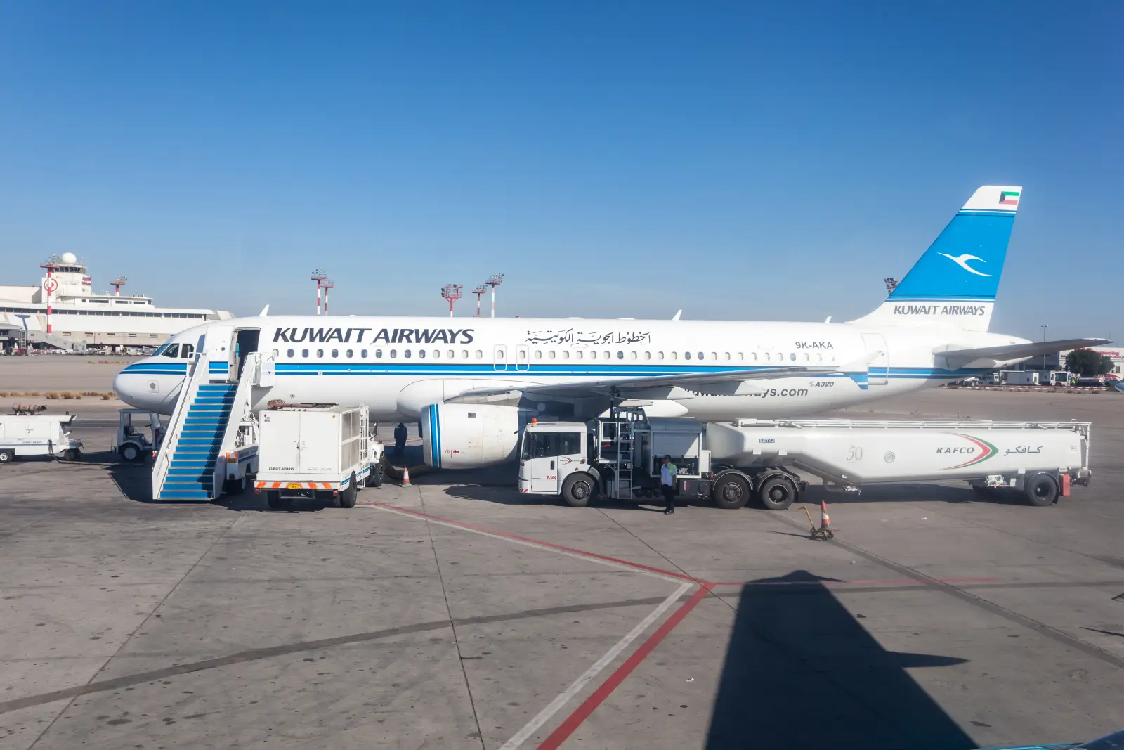 Kuwait Airways aircraft at Kuwait International Airport with ground services and refuelling equipment on the apron