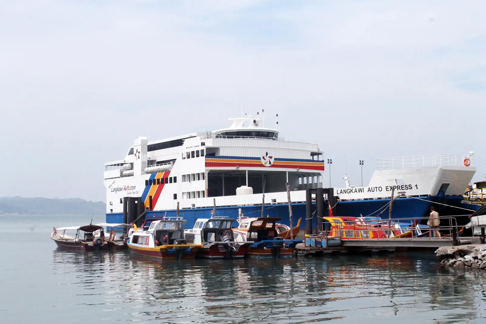 A large Langkawi Auto Express ferry docked at a calm harbor with small boats in the foreground