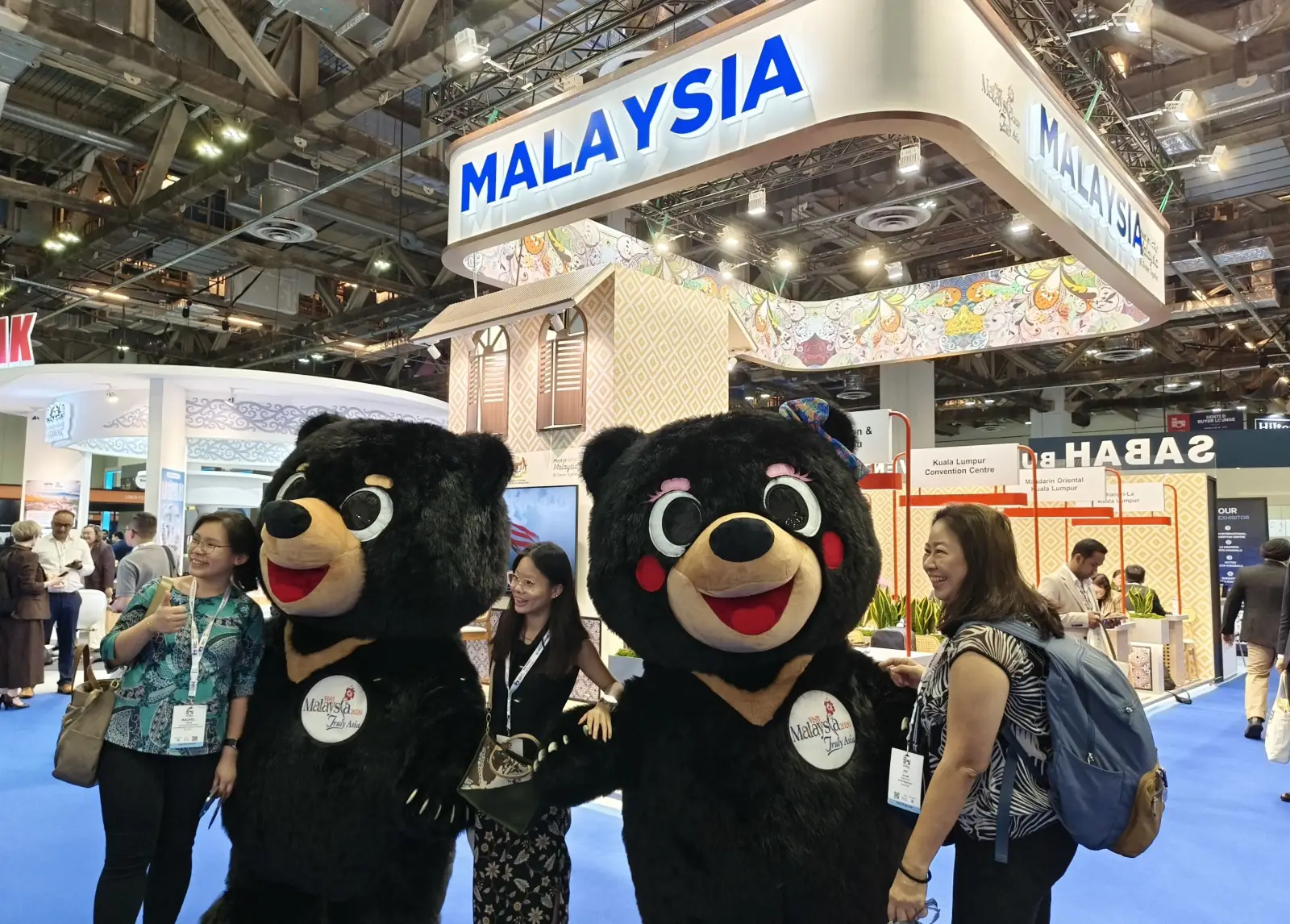 Malaysia pavilion at TMS APAC 2026 in Singapore with sun bear mascots posing with delegates at a busy MICE trade show stand