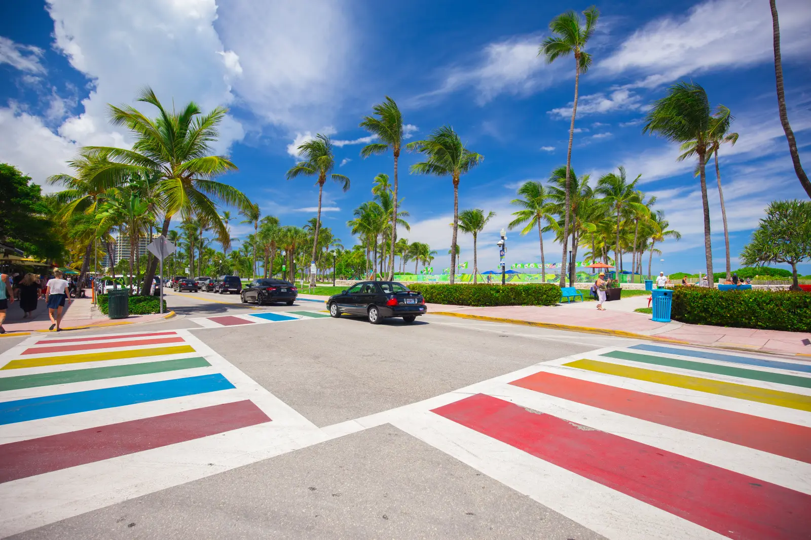 Rainbow crosswalk on Ocean Drive in Miami Beach with palm trees, blue sky, and beachfront promenade, highlighting LGBTQ+ friendly destination