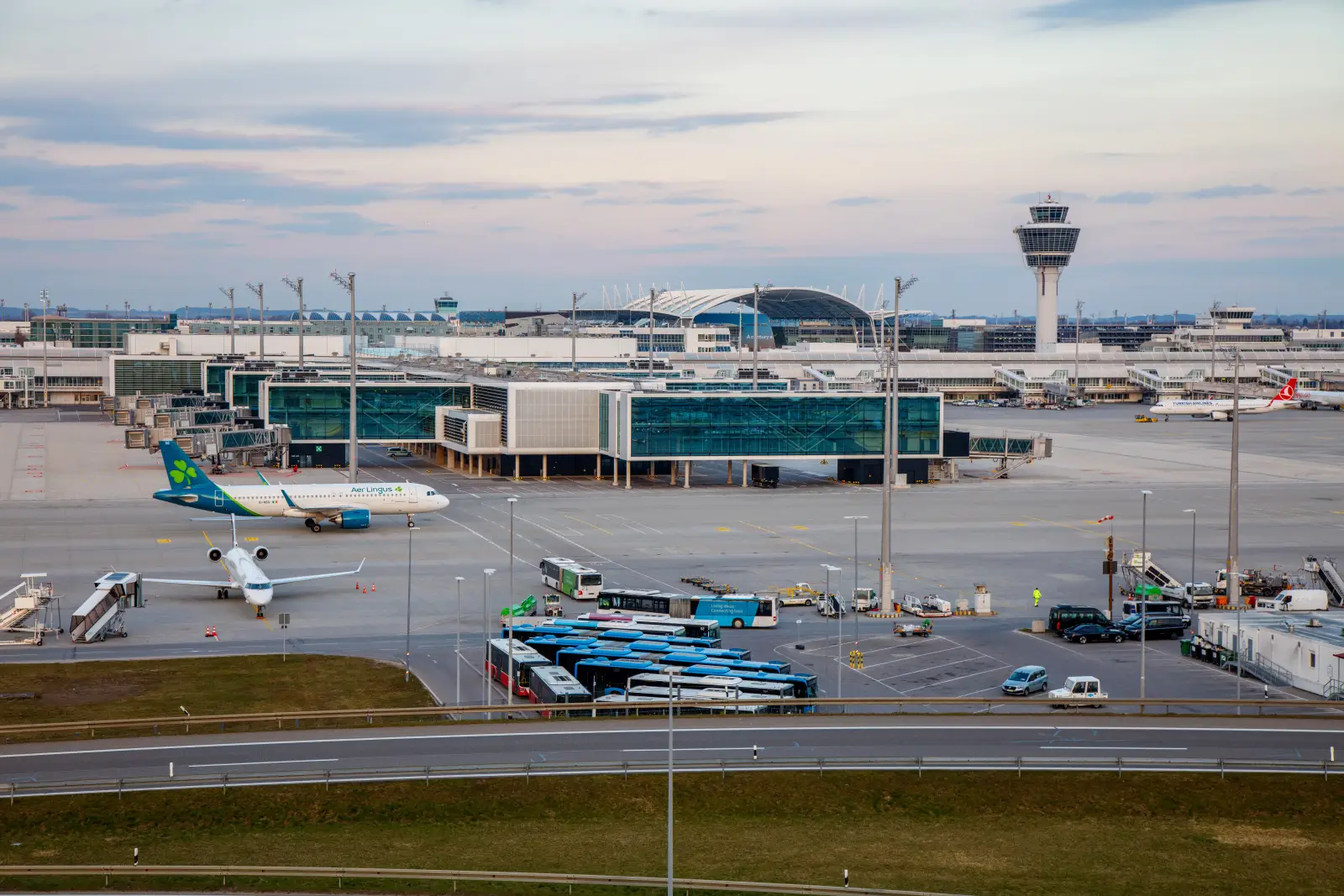 Munich Airport Terminal 1 pier exterior with aircraft at gates, apron operations, and control tower in the background