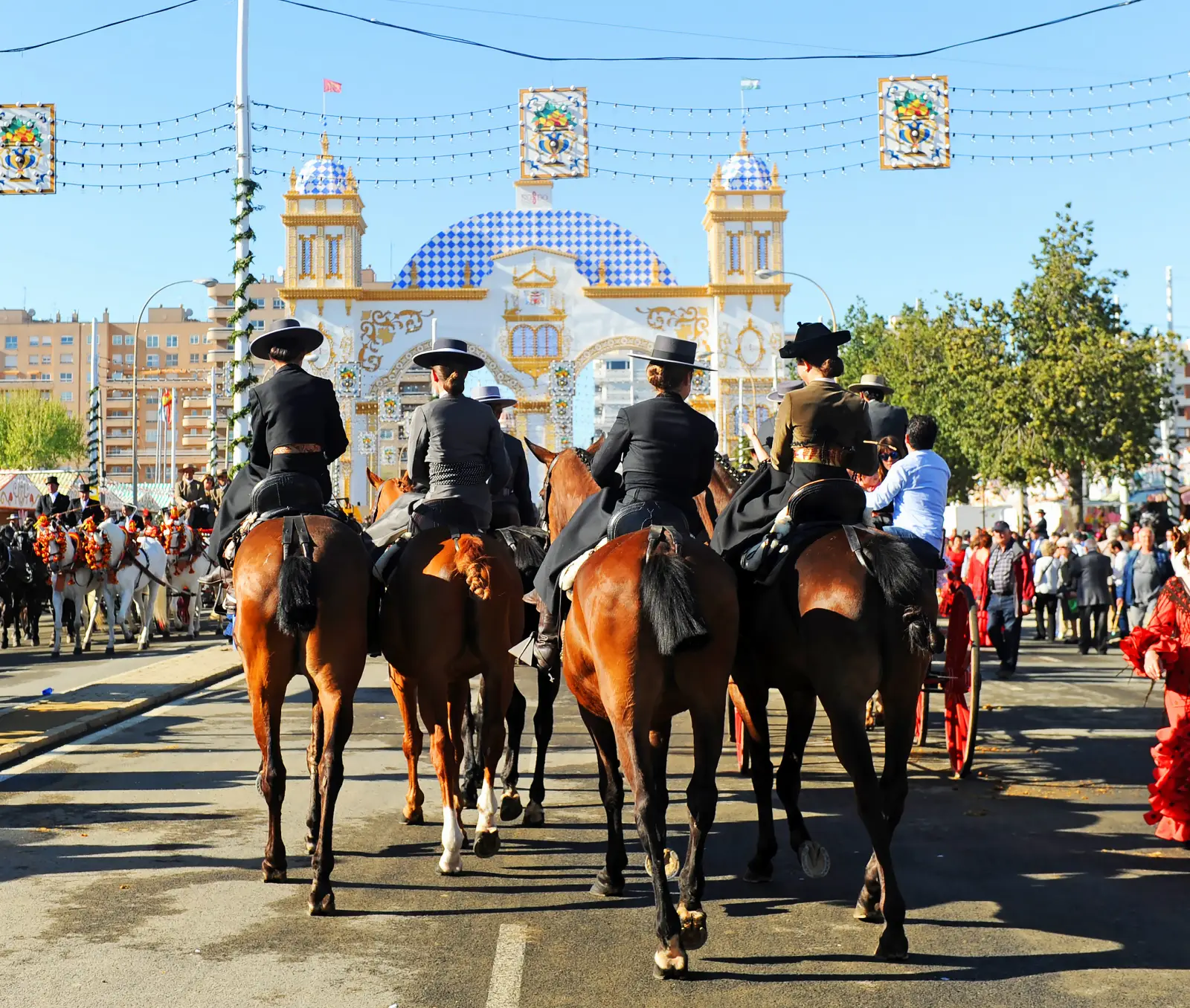 Riders on horseback in traditional dress at Seville April Fair passing decorated fair entrance in Andalusia Spain.