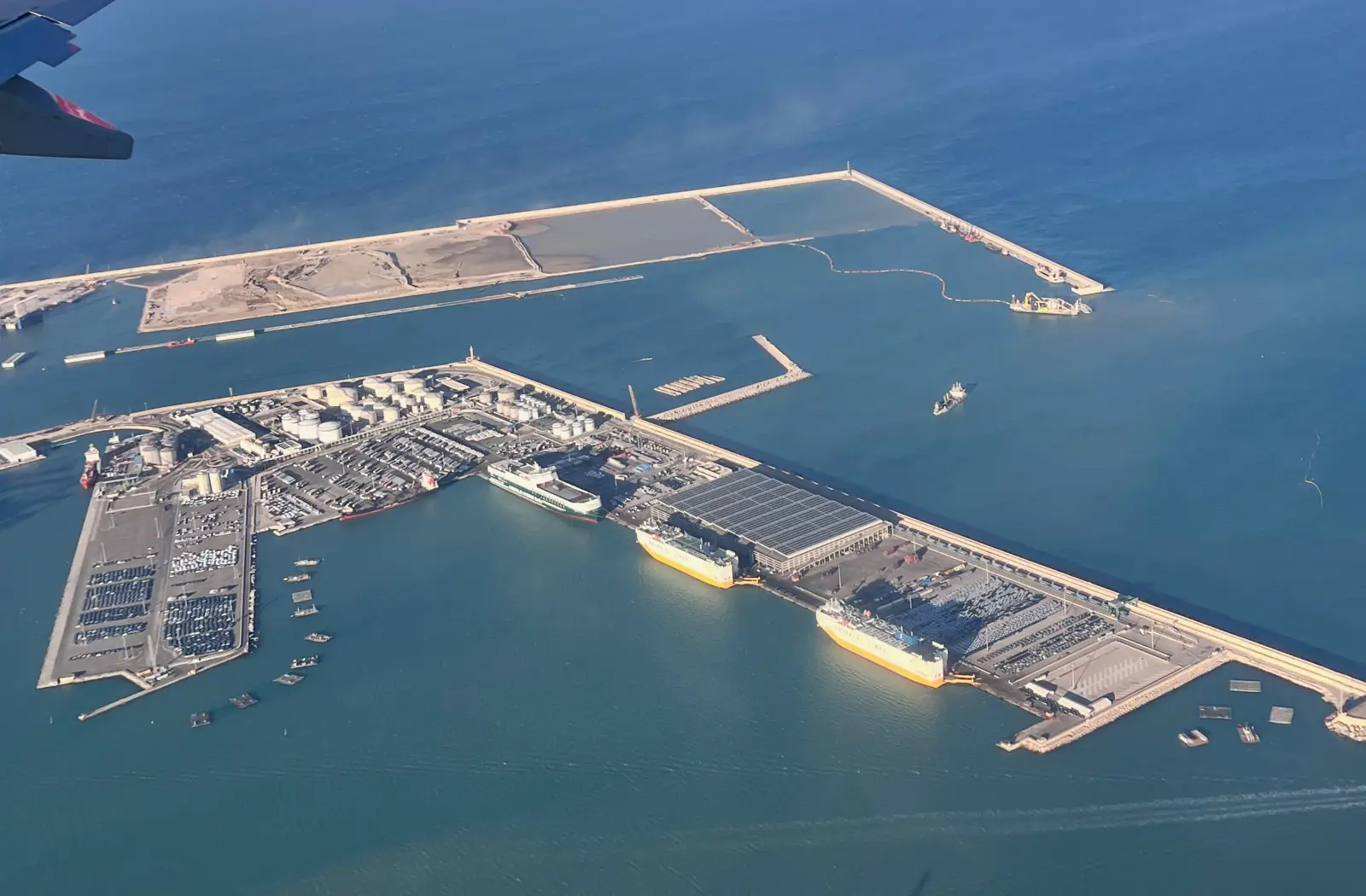 Aerial view of the Port of Valencia showing port infrastructure, ro-ro vessels at berth, vehicle storage areas and the northern extension under construction in the background
