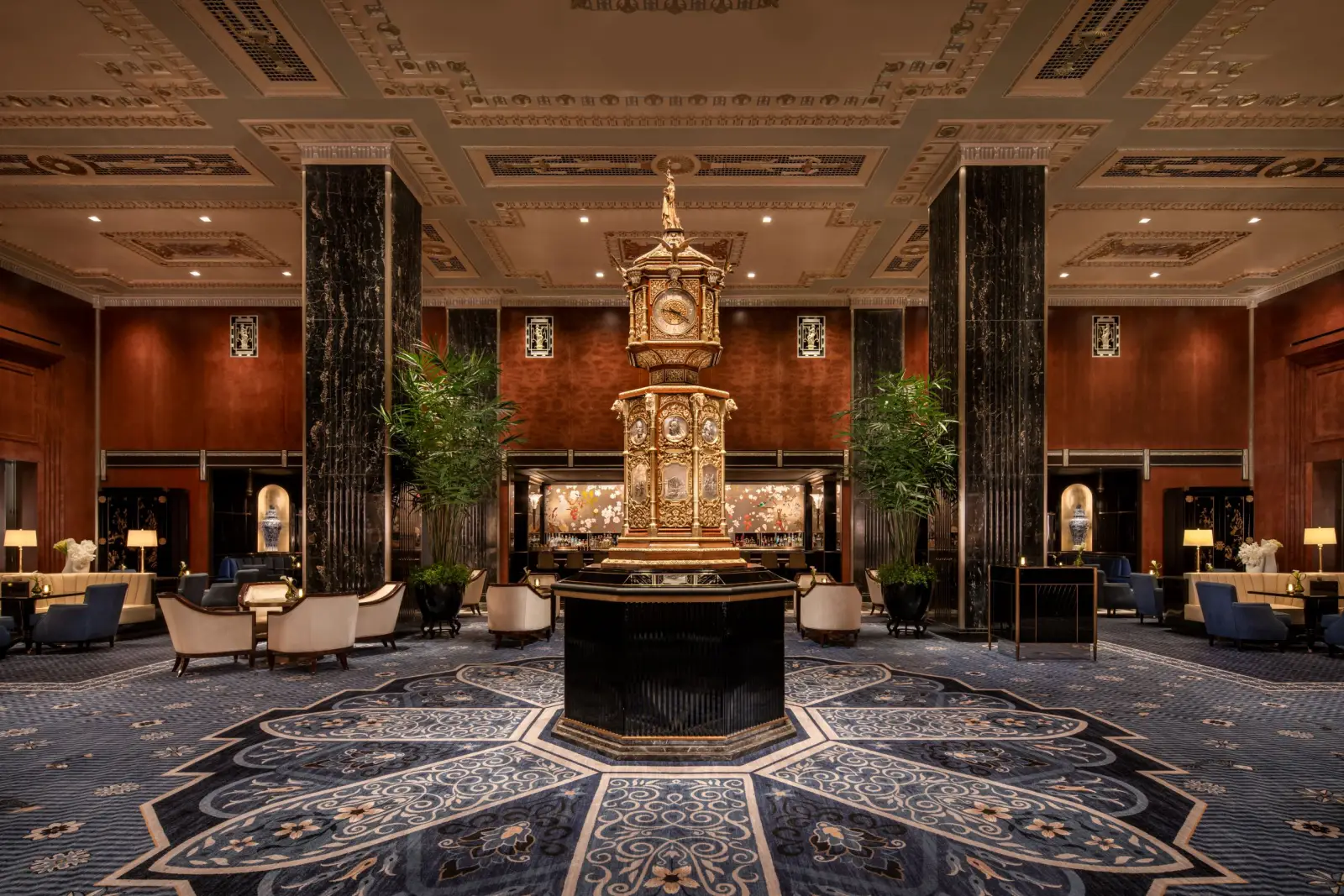 Restored Peacock Alley lobby at Waldorf Astoria New York with ornate central clock, marble columns, Art Deco ceiling details and luxury seating.