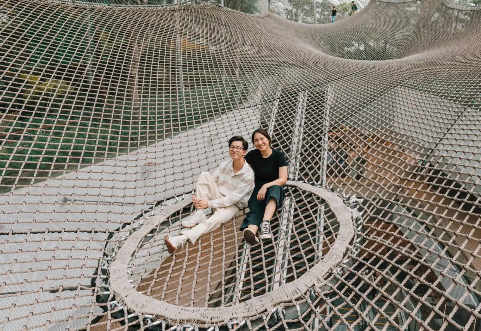 Jewel Changi Airport: Key Highlights Of This Iconic Lifestyle Destination (Part 2) 4 Two visitors sitting on the large rope Walking Net attraction at Canopy Park, Jewel Changi Airport, suspended high above the ground.
