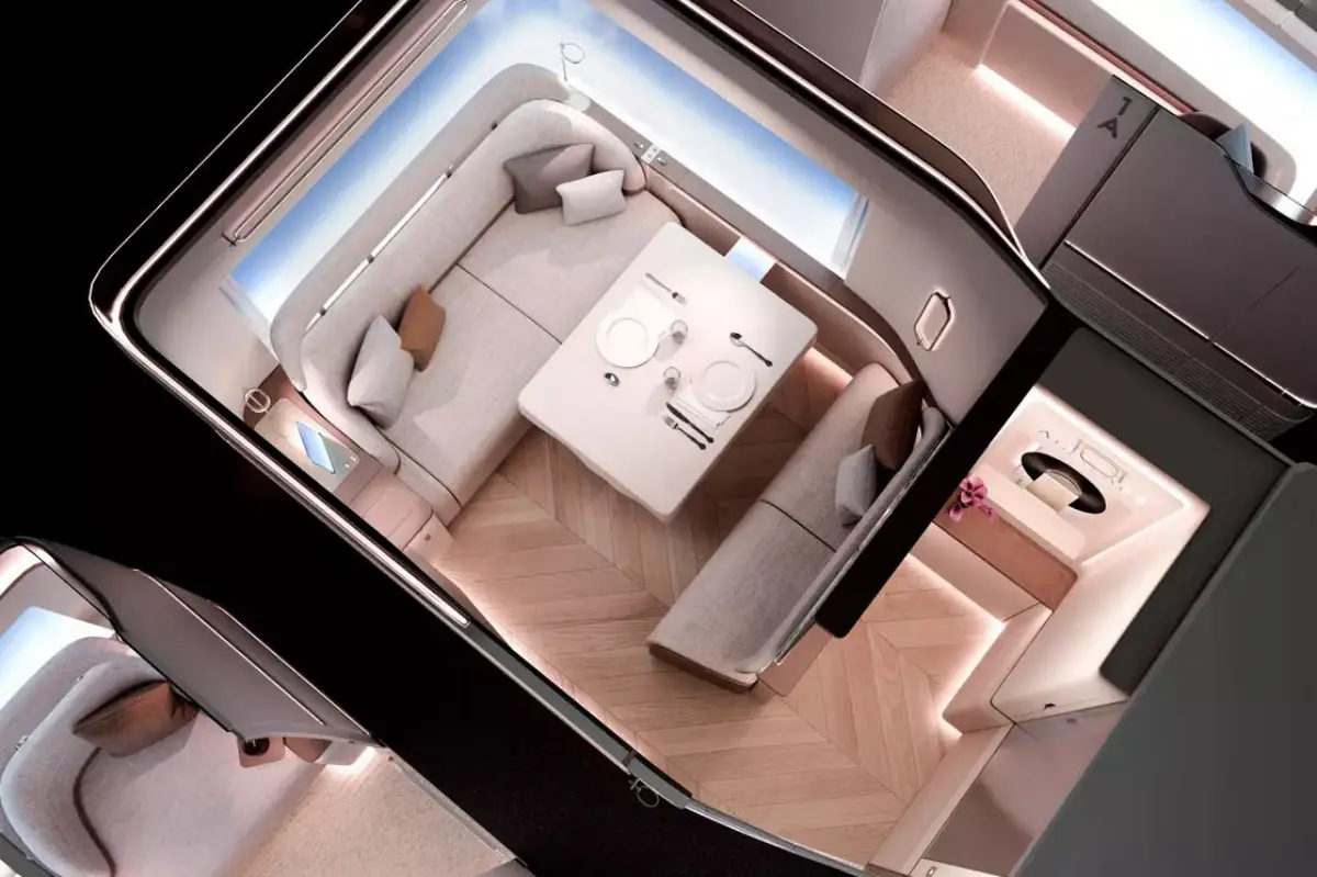 Overhead view of the Airbus A350-1000 First Class Master Suite concept, showing a spacious two-passenger suite with a herringbone wood floor, wraparound cream upholstered seating, a dining table set for two, soft ambient lighting, and a private lavatory visible to the right