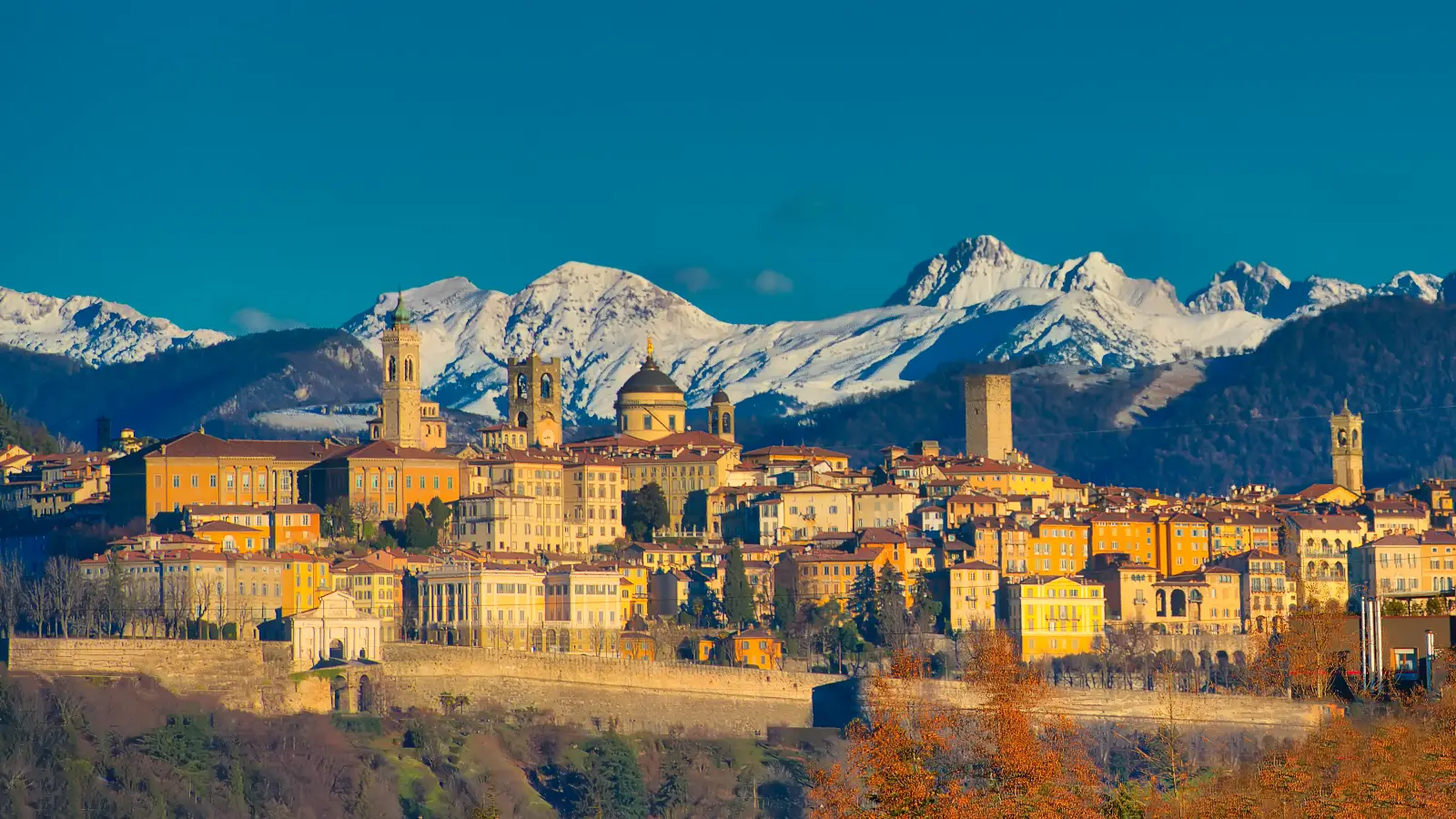 Snow-covered mountains rise behind Bergamo’s historic skyline in early morning sunlight
