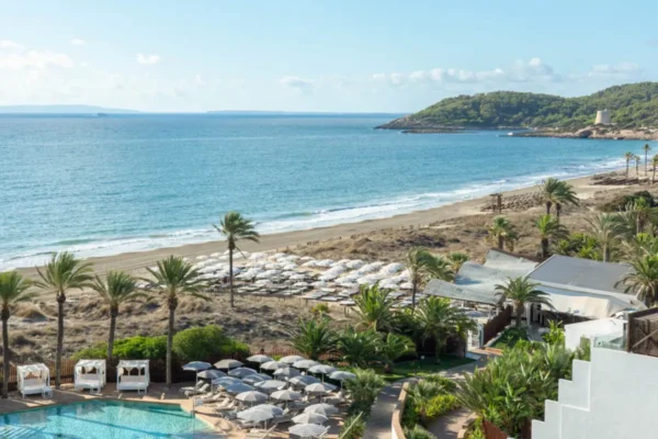 Beachfront view of Bless Ibiza The Site resort with pools, palm trees and Mediterranean coastline in Ibiza