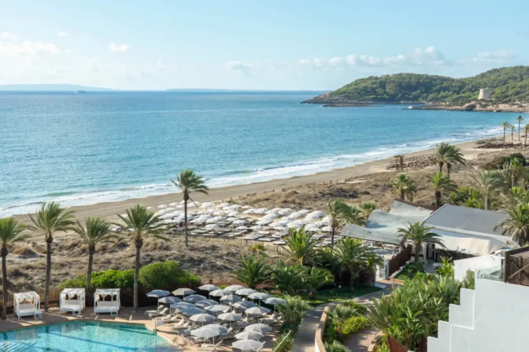 Beachfront view of Bless Ibiza The Site resort with pools, palm trees and Mediterranean coastline in Ibiza