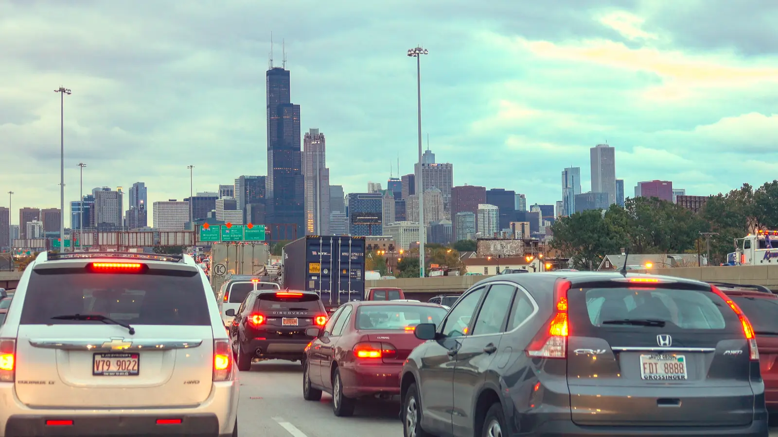 Heavy traffic entering downtown Chicago with cars on a busy expressway and the city skyline visible under cloudy skies.