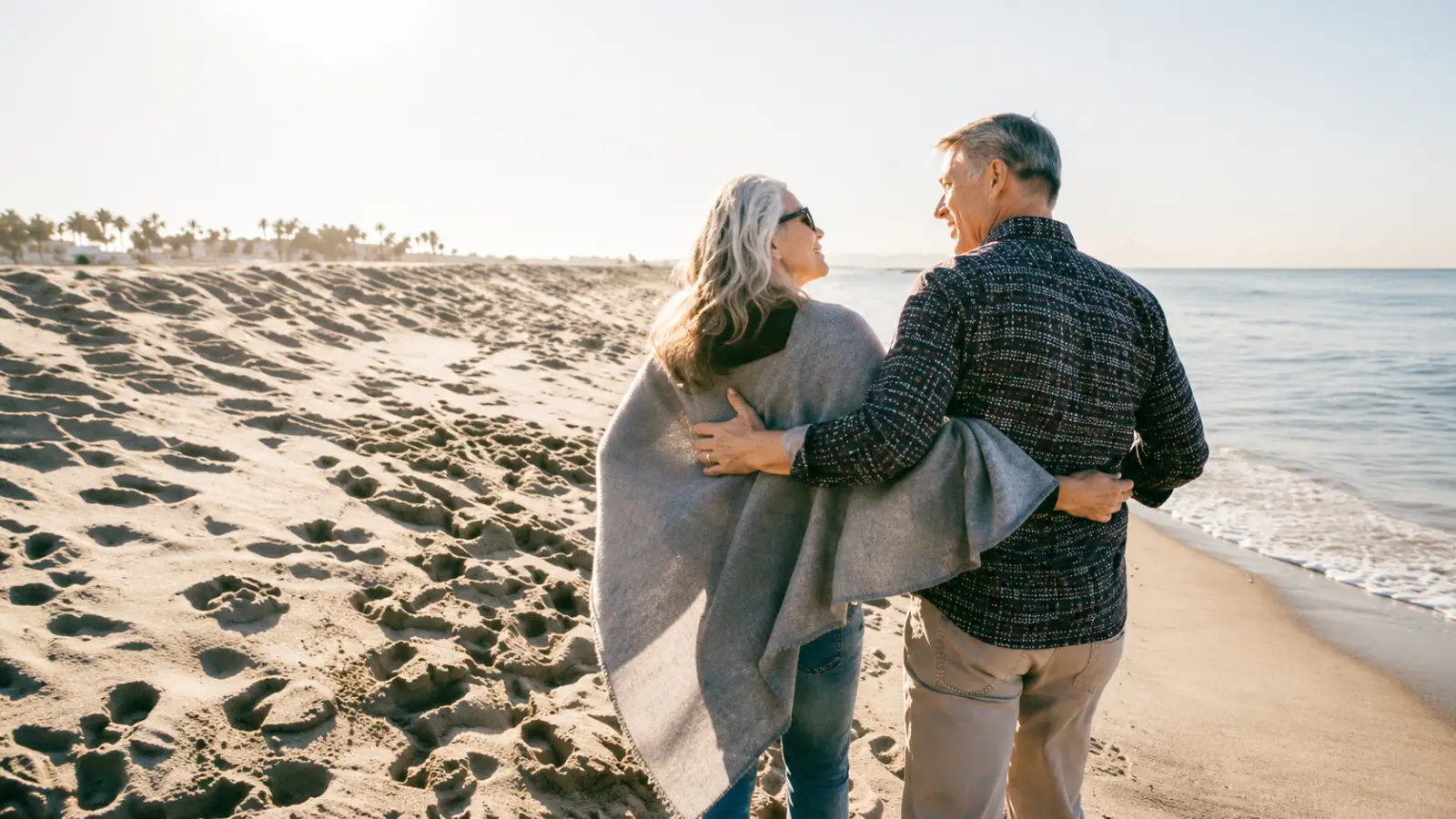 Older couple walking together on a sandy beach during a long-distance trip