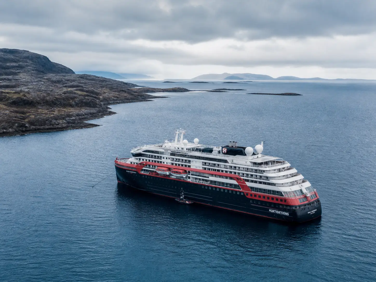 Expedition cruise ship anchored in Atlantic Ocean near rugged coastline under overcast sky