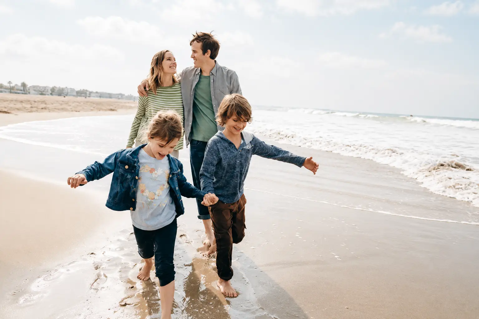 Family with two children walking barefoot along a sandy beach during a relaxed seaside holiday