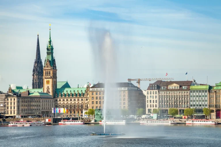 Historic skyline of Hamburg, Germany, with the city hall, church spires and fountain on the Alster Lake under a clear sky.