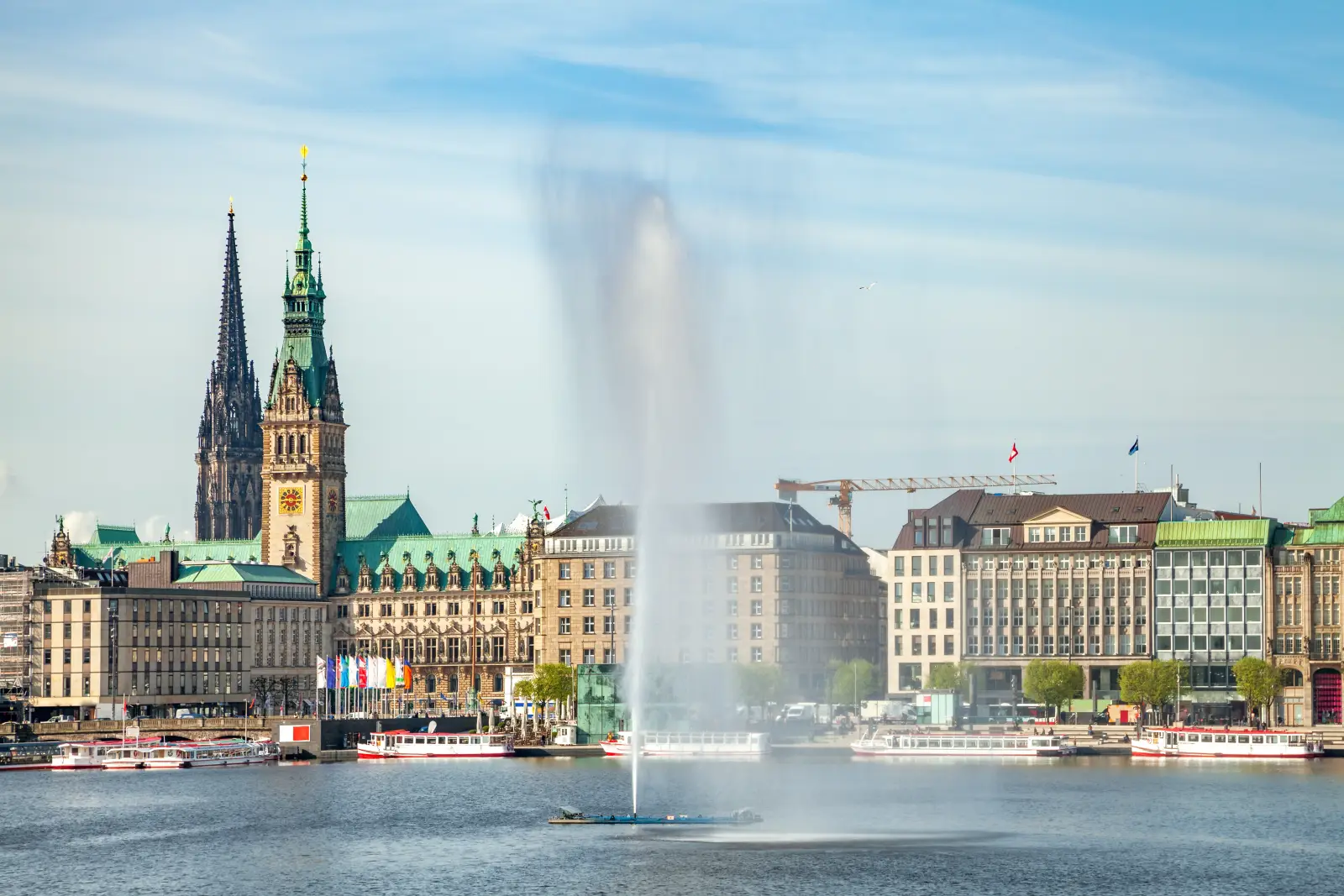 Historic skyline of Hamburg, Germany, with the city hall, church spires and fountain on the Alster Lake under a clear sky.