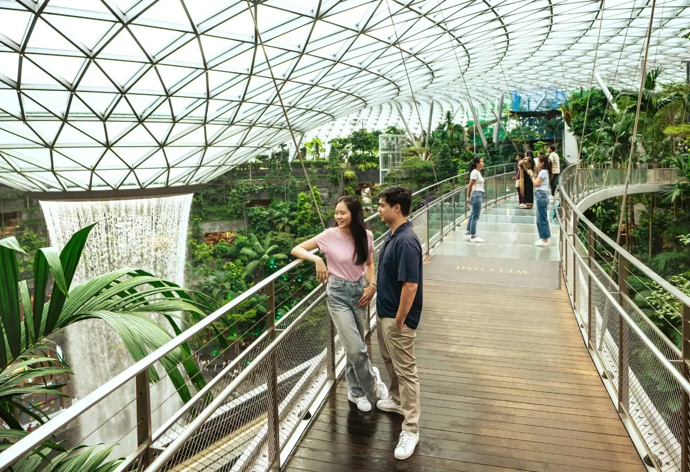 Jewel Changi Airport: Key Highlights Of This Iconic Lifestyle Destination (Part 1) 4 Visitors walk along the Canopy Bridge inside Jewel Changi Airport overlooking the Rain Vortex waterfall and indoor garden in Singapore
