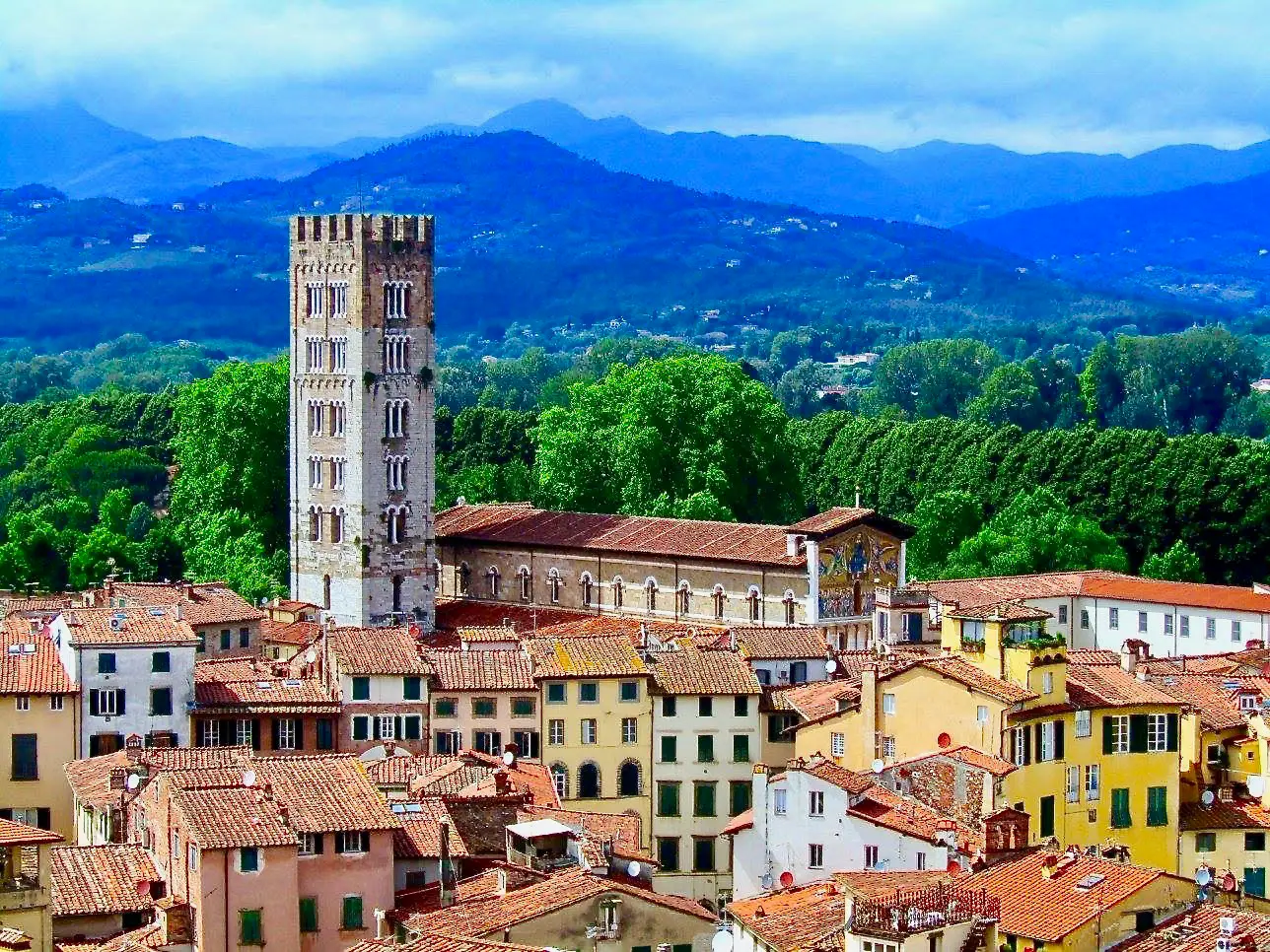 Panoramic view of Lucca’s historic center with medieval tower, terracotta rooftops and Tuscan hills in the background.