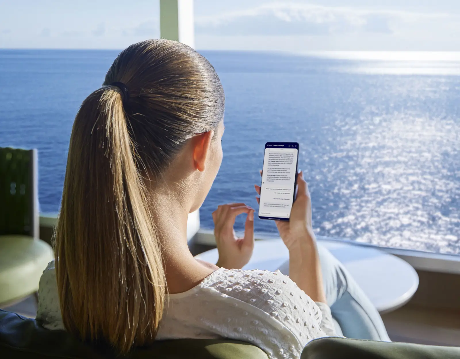 Cruise passenger uses the MSC Cruises AI Concierge app on a smartphone while relaxing aboard a ship with ocean views in the background.