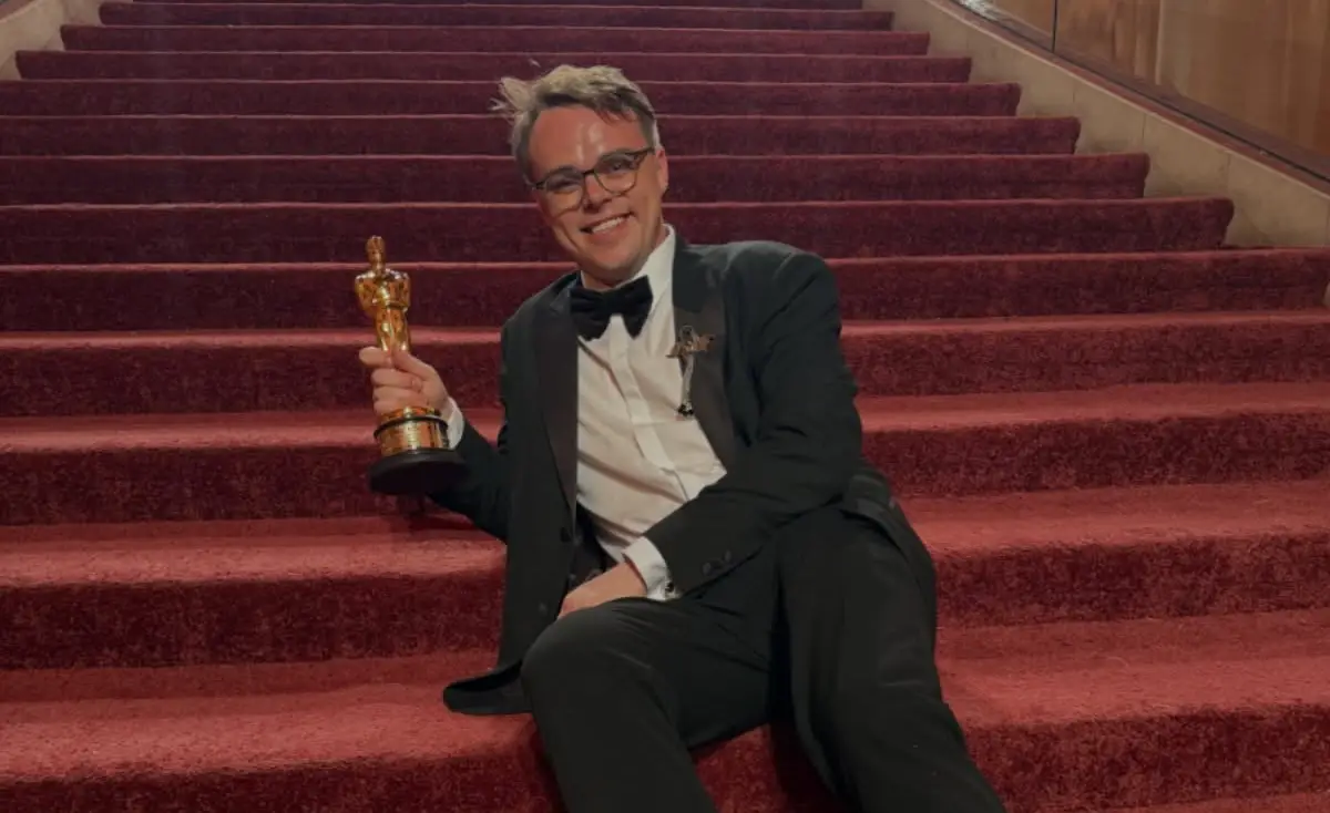 Pavel Talankin, co-director of Mr. Nobody Against Putin, sits smiling on red-carpeted theatre steps in a black tuxedo and bow tie, holding his gold Academy Award statuette after winning the Best Documentary Feature award at the 2026 Academy Awards