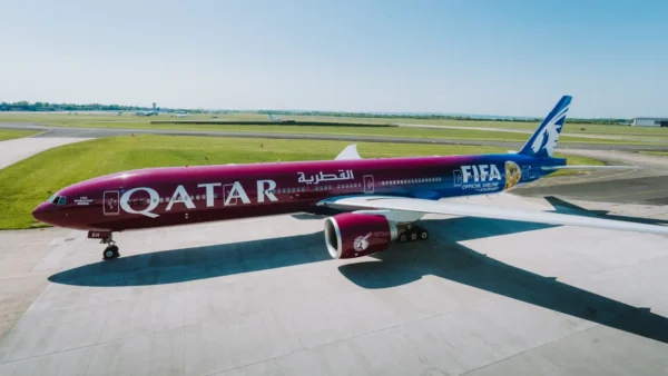 A Qatar Airways Boeing 777 on the tarmac displaying the FIFA World Cup 2026 special livery, with a deep red-to-blue gradient design featuring the Qatar Airways and FIFA branding along the fuselage