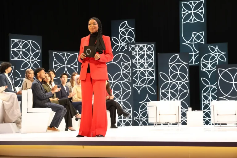 Qatar cultural event stage in Canada featuring a presenter in a red suit speaking during a Doha Debates programme