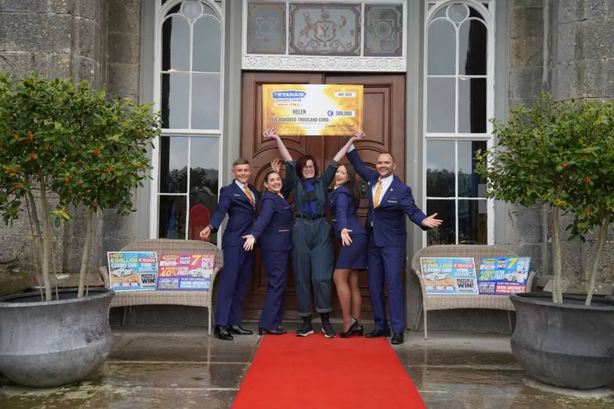 Helen Swindells, dressed in dark casual clothing, stands at the entrance of Slane Castle in Ireland, raising a large ceremonial cheque for 500,000 euros above her head alongside four Ryanair cabin crew members in navy uniforms. A red carpet leads to the castle door, and Ryanair scratch card promotional displays are visible on either side.