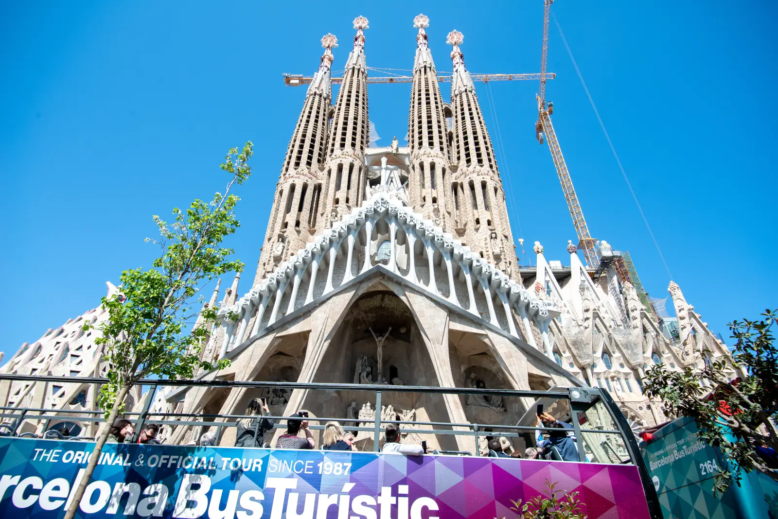 Tourists on Barcelona sightseeing bus passing Sagrada Familia under clear blue sky