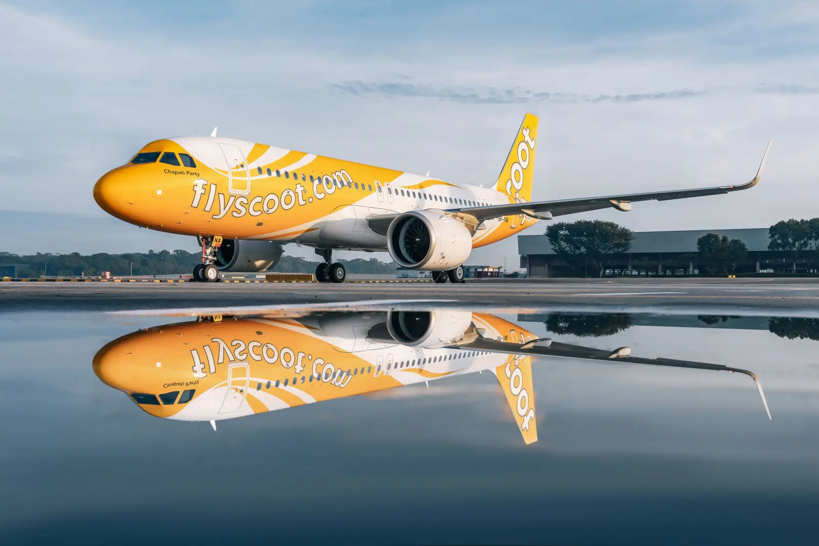 Scoot Airbus A320neo aircraft parked on the tarmac with a reflection on wet ground at Singapore Changi Airport.