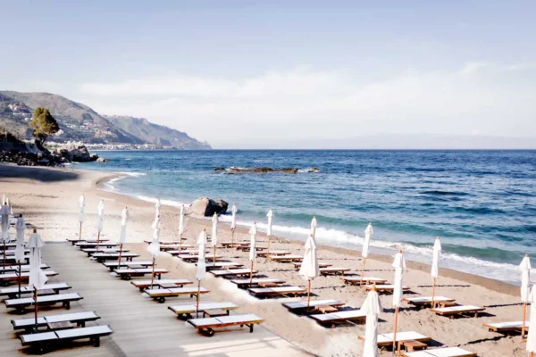 Sun loungers and white umbrellas lined along the beach at a Taormina beach club on the Sicilian coast