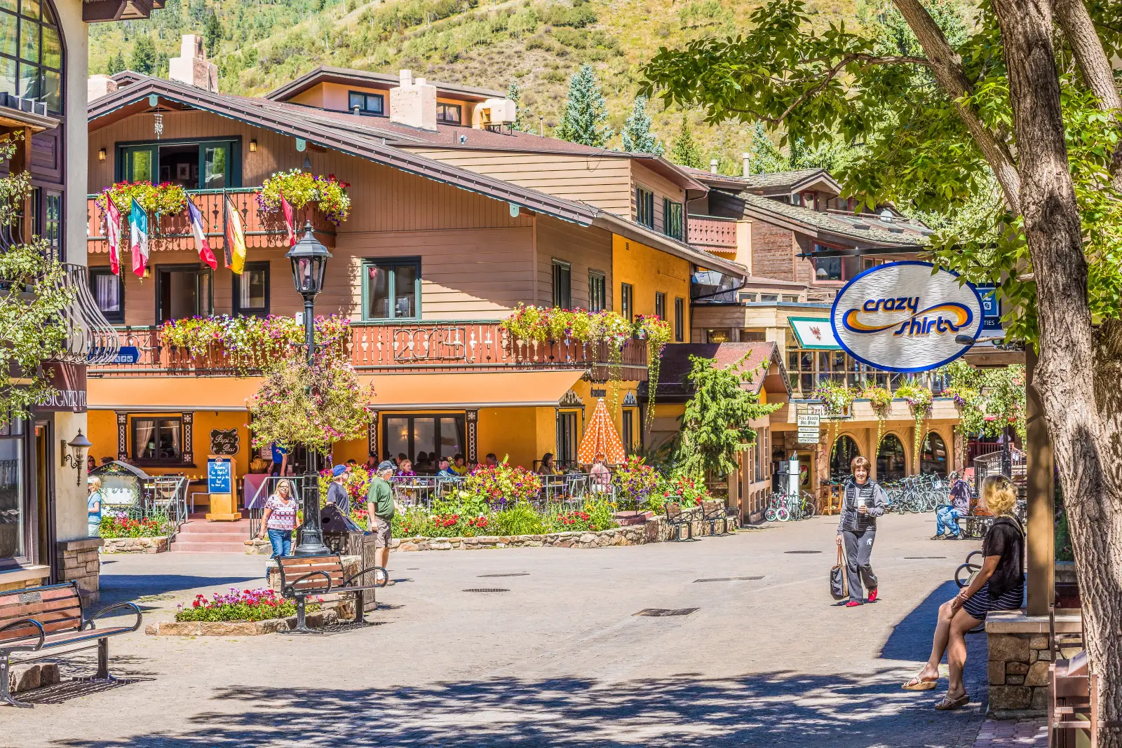 Pedestrian street in Vail, Colorado, lined with Swiss-style buildings, flower balconies, shops, and tourists on a sunny day.