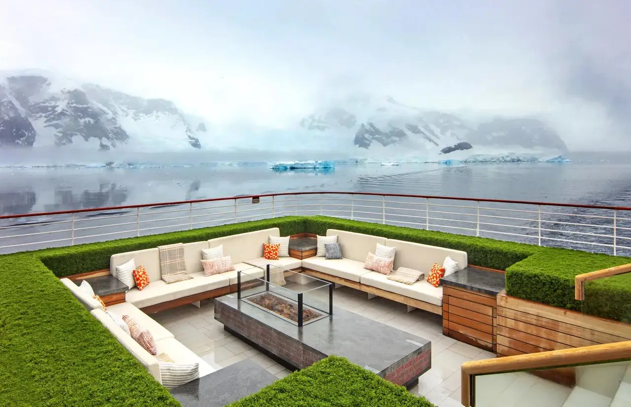 Outdoor lounge deck aboard a Viking expedition cruise ship sailing through Antarctica with glaciers and snow-covered mountains in the background.