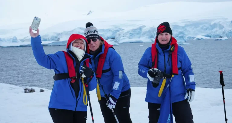 Cruise Travel 34 Women travelers in blue expedition jackets take a selfie on the snowy Antarctic coastline during an Aurora Expeditions cruise.