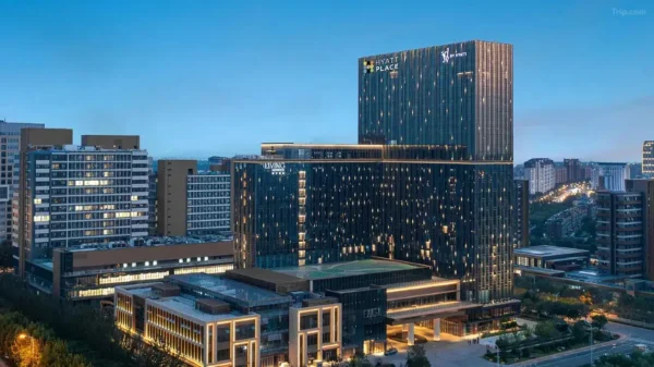 Aerial dusk view of Hyatt Place Tianjin South Railway Station, a tall dark-glass tower with illuminated Hyatt Place signage, set within a large mixed-use development surrounded by city buildings and lit streets.