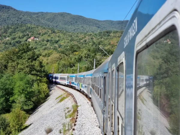 ALT text: Retro Istria Express passenger train traveling through a forested mountain landscape on a curved railway line in Central Europe.